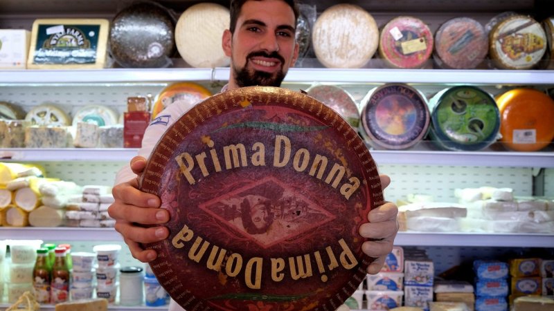 An Israeli vendor holding a Dutch Prima Donna cheese at Basher Fromagerie cheese shop in Mahane Yehuda West Jerusalem Israel|Uzi-Eli Chezi