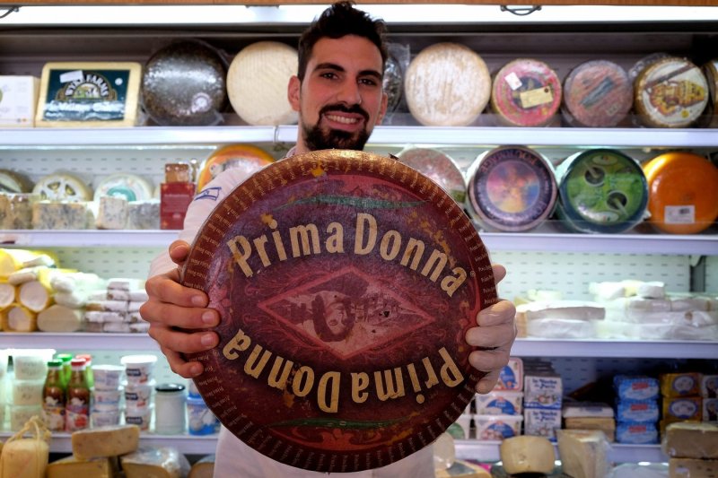 An Israeli vendor holding a Dutch Prima Donna cheese at Basher Fromagerie cheese shop in Mahane Yehuda West Jerusalem Israel|Uzi-Eli Chezi