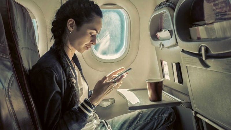 52082765 - woman sitting at airplane and looking to mobil phone.|