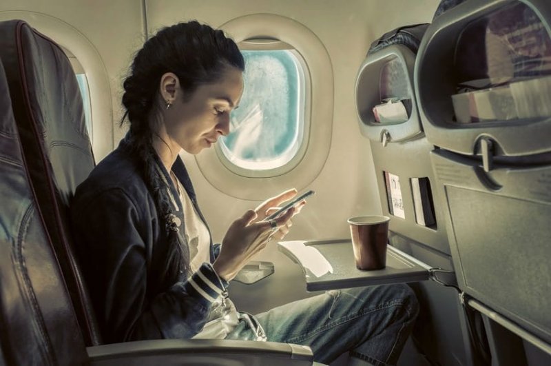 52082765 - woman sitting at airplane and looking to mobil phone.|